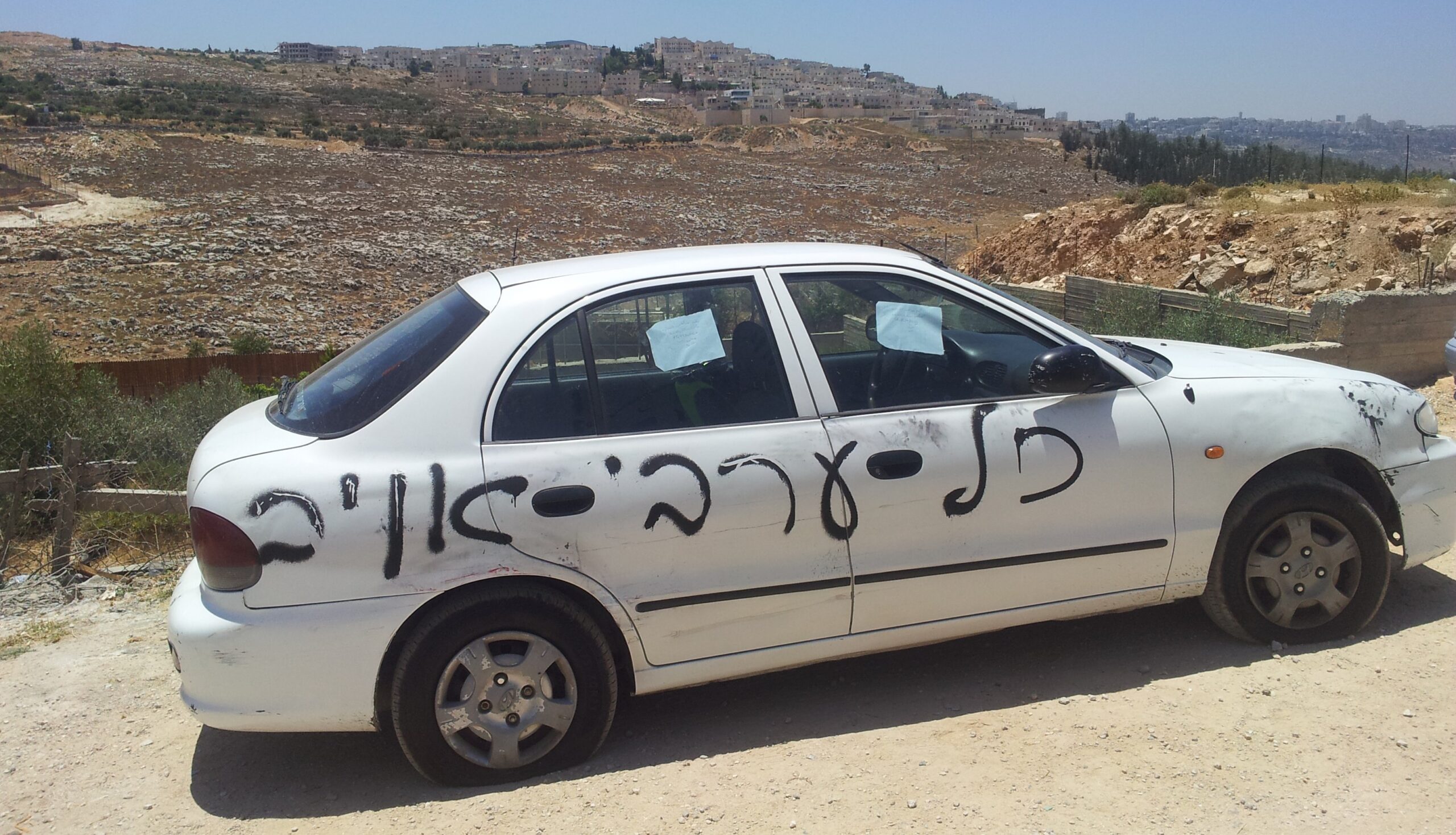 Muhammeds bil där israeliska extremister har punkterat däcken och sprayat ”Alla araber är fienden”. I bakgrunden kan man se en israelisk bosättning.