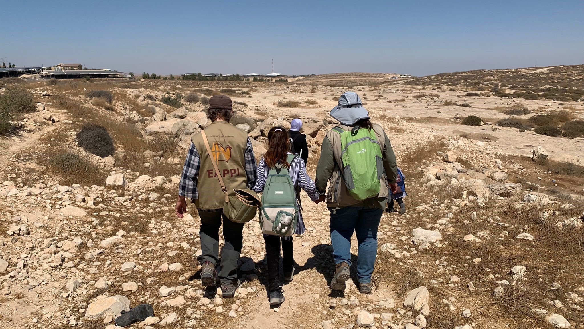 Följeslagare håller skolbarnen i handen på väg hem från skolan till byn.